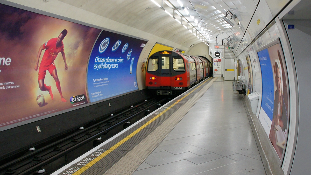 A train arriving at Embankment station with cross track and platform level adverts visible