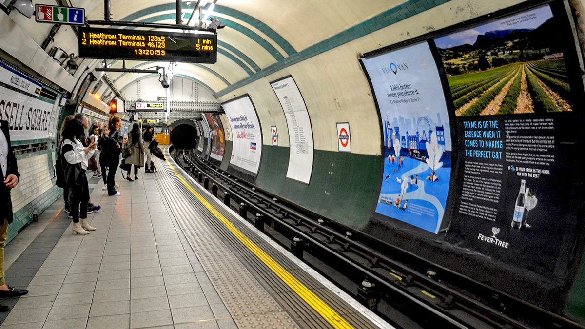 Commuters looking at 16 sheet cross track advert whilst waiting for their train at Russell Square tube station