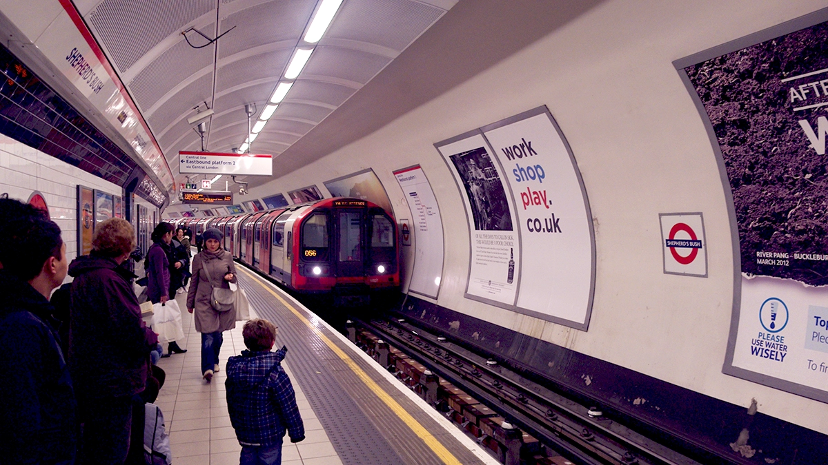 Commuters wait for their train to stop across from platform adverts at Shepherd's Bush underground station