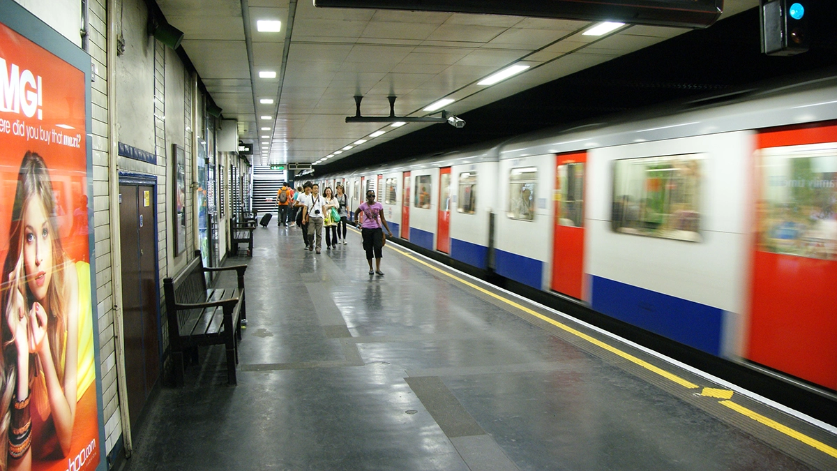 A tube train leaving the station at St. James's Park with passengers leaving past platform adverts