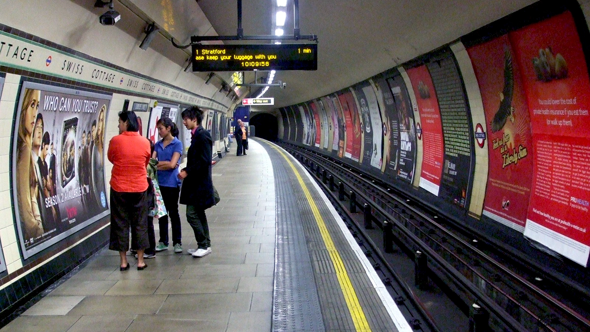 A group of commuters study a 12 sheet platform poster at Swiss Cottage tube station